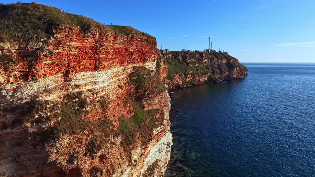 Penhascos com vista para a água azul em uma área costeira com um farol ao longe durante um dia ensolarado no início da tarde