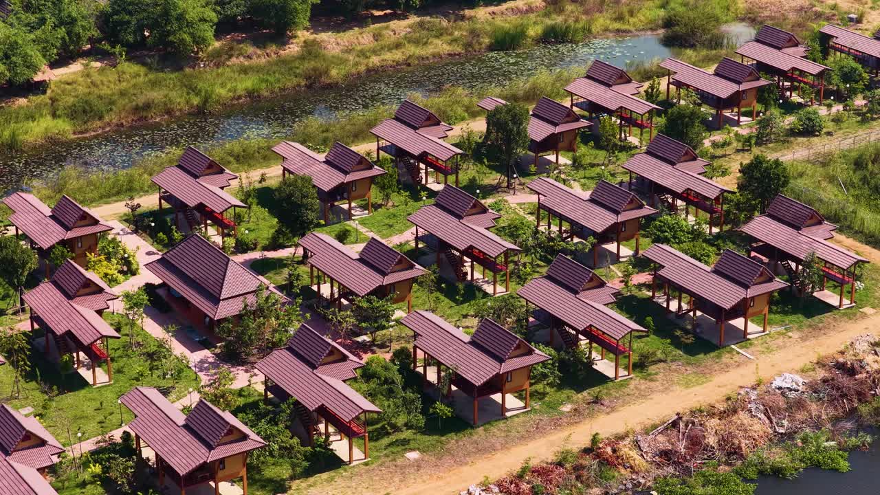 Bidikan drone sudut tinggi menangkap deretan bungalow kayu tradisional di tepi sungai di bawah sinar matahari yang cerah