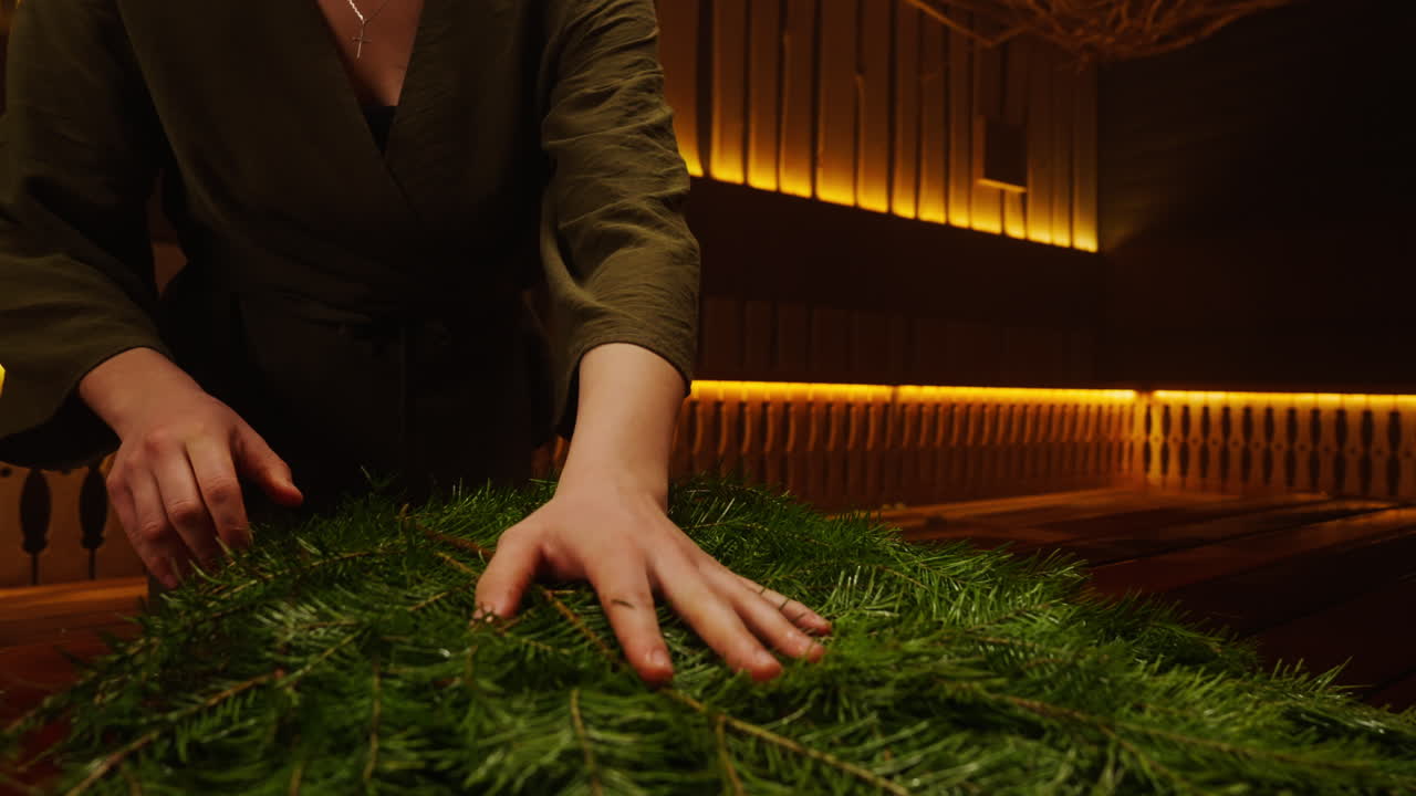 Woman arranging fir branches in a wooden spa setting