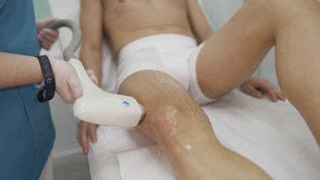 professional therapist makes laser hair removal on man's leg in beauty salon