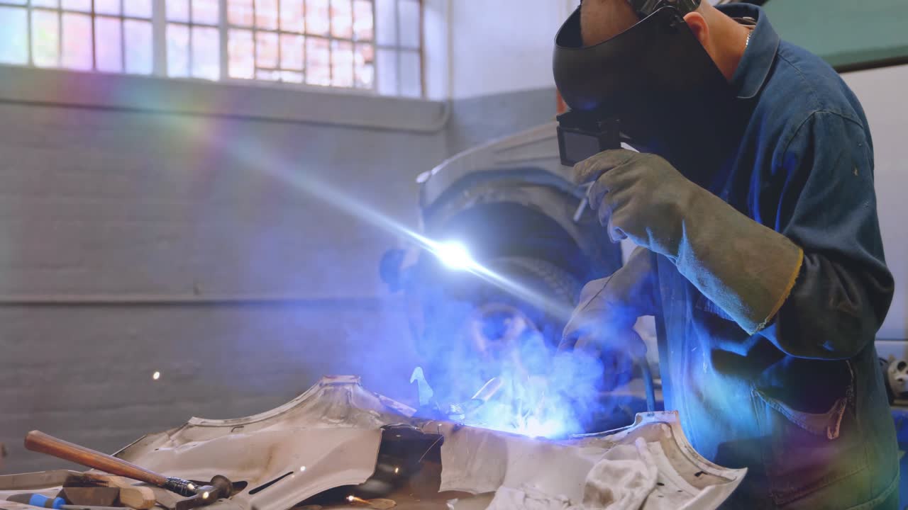 Auto body technician raising welding torch on dented panel guiding animated sparks repairing seam