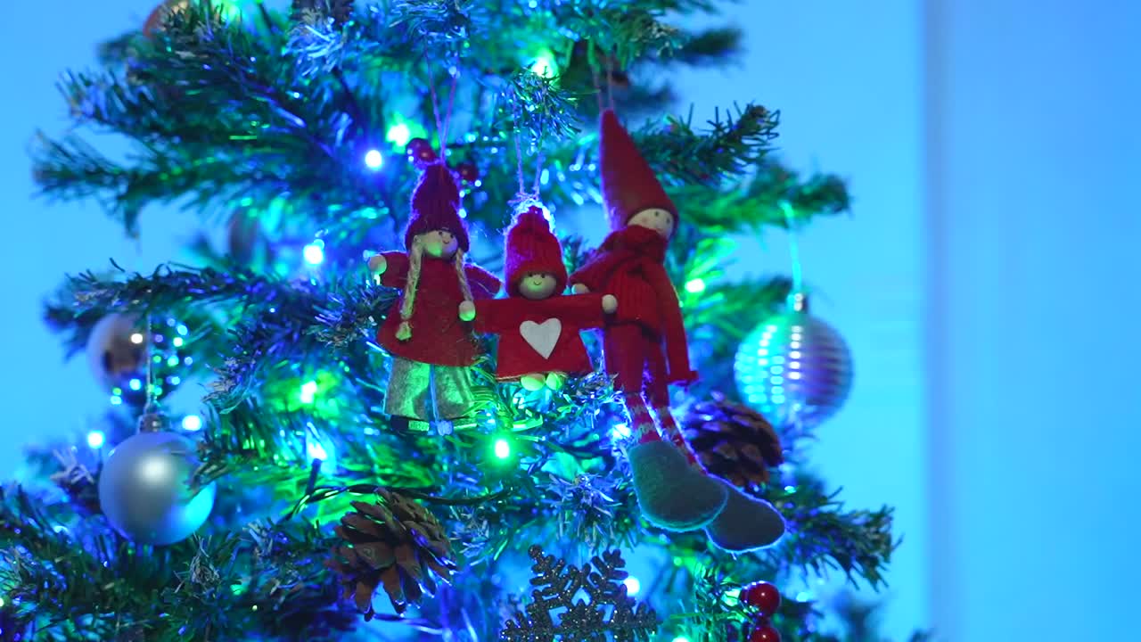 Woman finishes placing a child ornament next to the parent figures on the Christmas tree at night