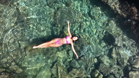 A-female-model-in-a-swimsuit-unwinds-in-a-small-pool-embraced-by-volcanic-rocks-along-the-ocean's-edge