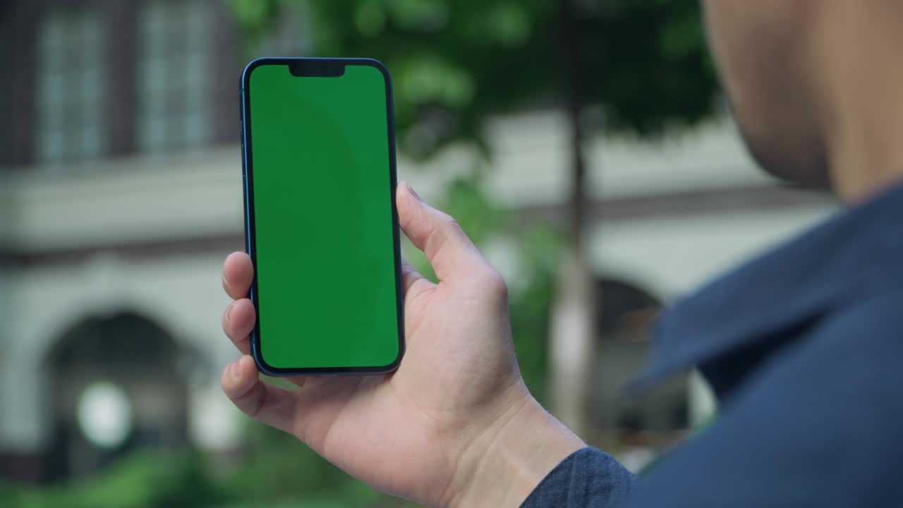 hombre de 4k de pie en la calle en la ciudad sosteniendo un teléfono inteligente con pantalla de maqueta verde