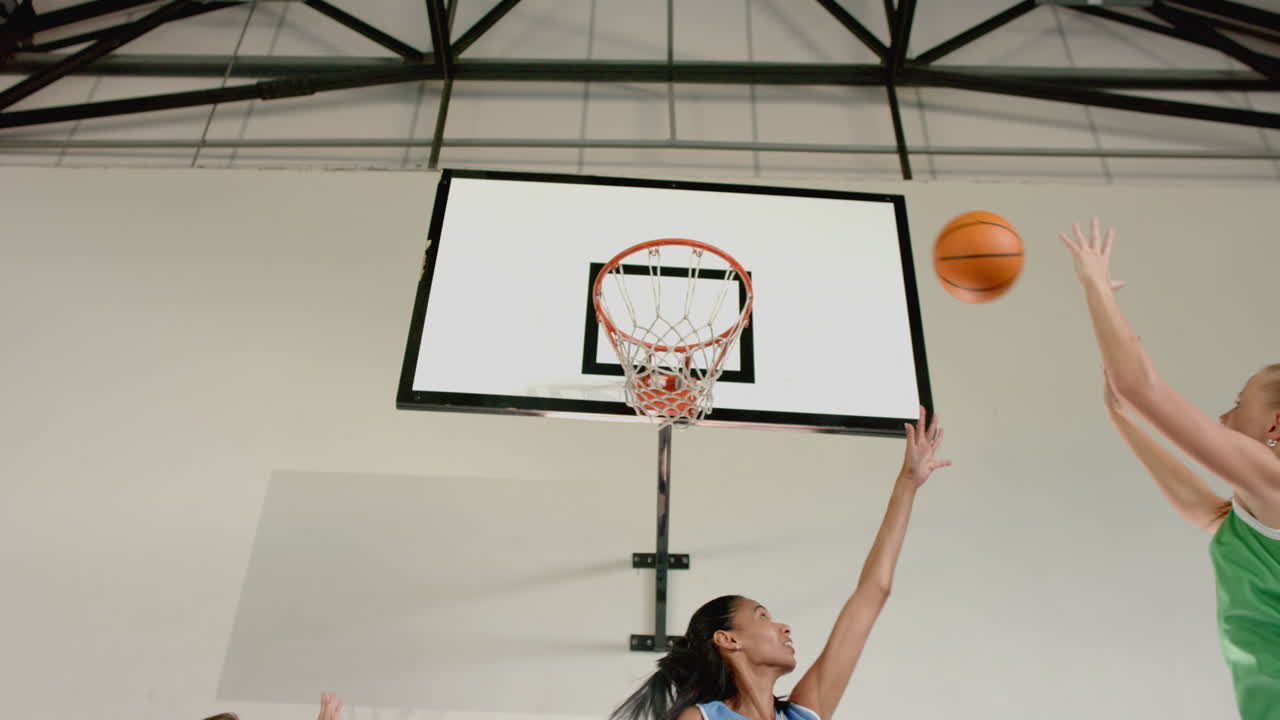 Playing basketball, women reaching for ball near hoop in indoor court