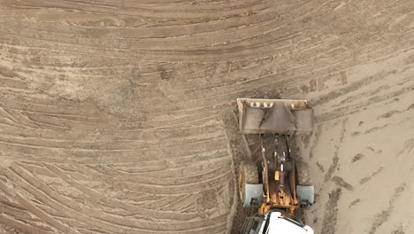 aerial view of a green construction crane moving soil on a construction site, creating a dust cloud