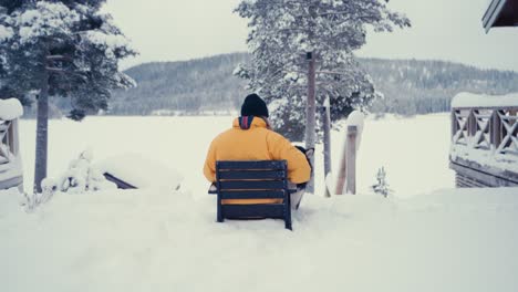 Hombre-Con-Chaqueta-Amarilla-Con-Su-Perro-Malamute-De-Alaska-Sentado-Afuera-Del-Patio-Cubierto-De-Nieve