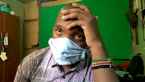 Powerless african man sitting at home and wearing face mask. Depressive Man with headache. Close up shot.