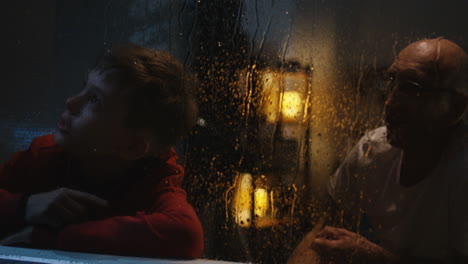 grandfather and grandchild watching rain at night