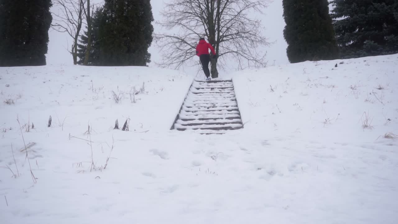 빨간 후드티와 검은색 바지를 입은 청년이 겨울에 밖에서 계단을 뛰어 오르고 있다