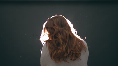 Young-woman,-teenager-with-long-hair,-shakes-her-head-delicately-over-the-light