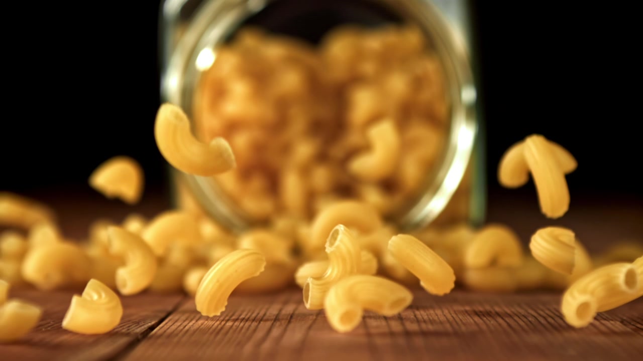 Maccheroni secchi che cadono su un tavolo di legno al rallentatore
