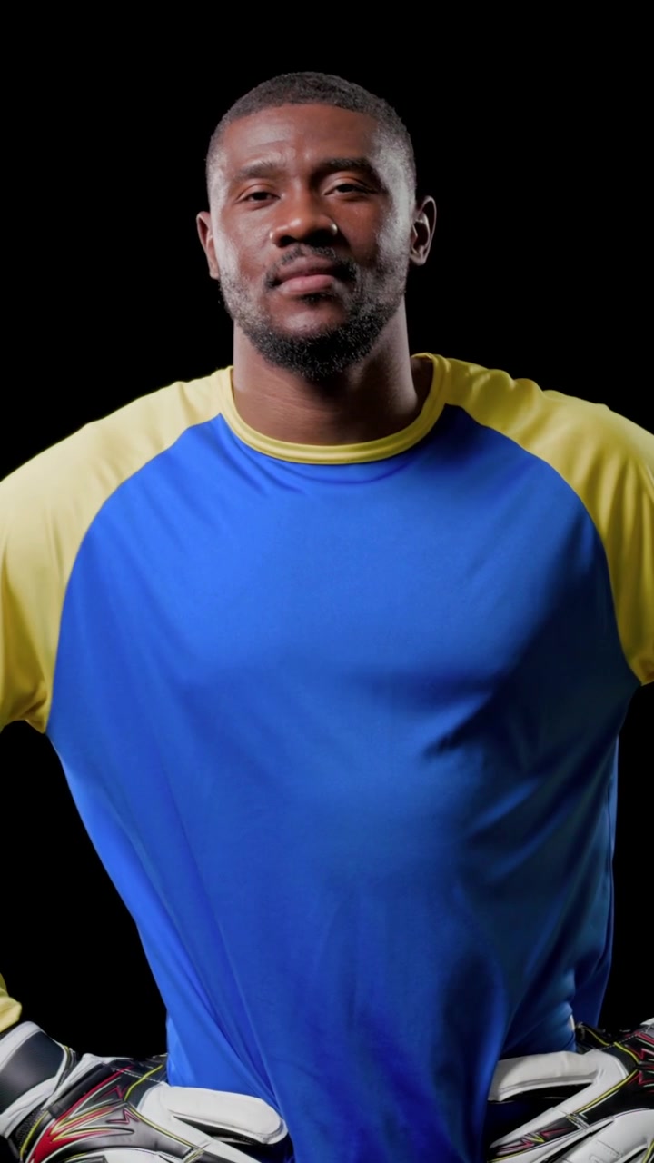 Video vertical: Cámara haciendo zoom, mostrando a un portero con camiseta azul manteniendo una pose para un anuncio de estudio con guantes.