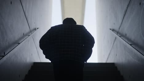 follow man silhouette wallking up staircase with concrete walls, slow motion
