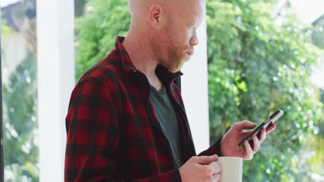 hombre albino afroamericano con rastas usando un teléfono inteligente y mirando por la ventana