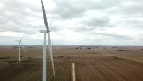 Bajando-La-Vista-Aérea-De-Un-Patio-De-Granja,-Campos-Y-Turbinas-Eólicas-Que-Se-Apagan-En-Un-Día-Nublado-De-Primavera-En-El-Centro-sur-De-Nebraska