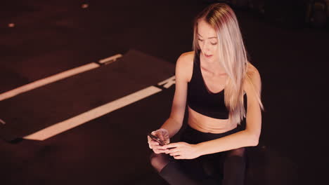 Lockdown-Shot-Of-Young-Woman-Using-Smartphone-While-Relaxing-On-Floor-After-Workout-Session