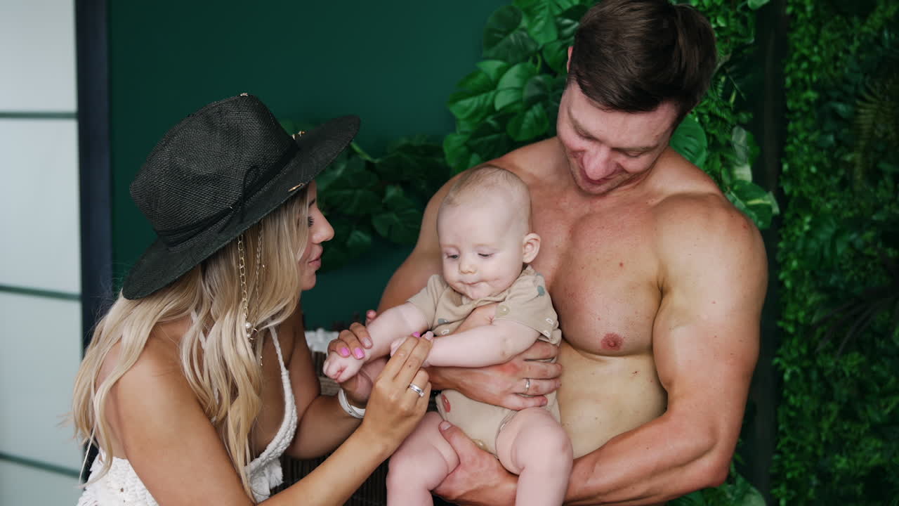 Young Caucasian parents are on vacation with their infant. Father holds his tiny son and mom holds kid's hands.