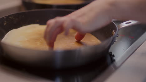 close-up of hand touching pancake in pan while baking