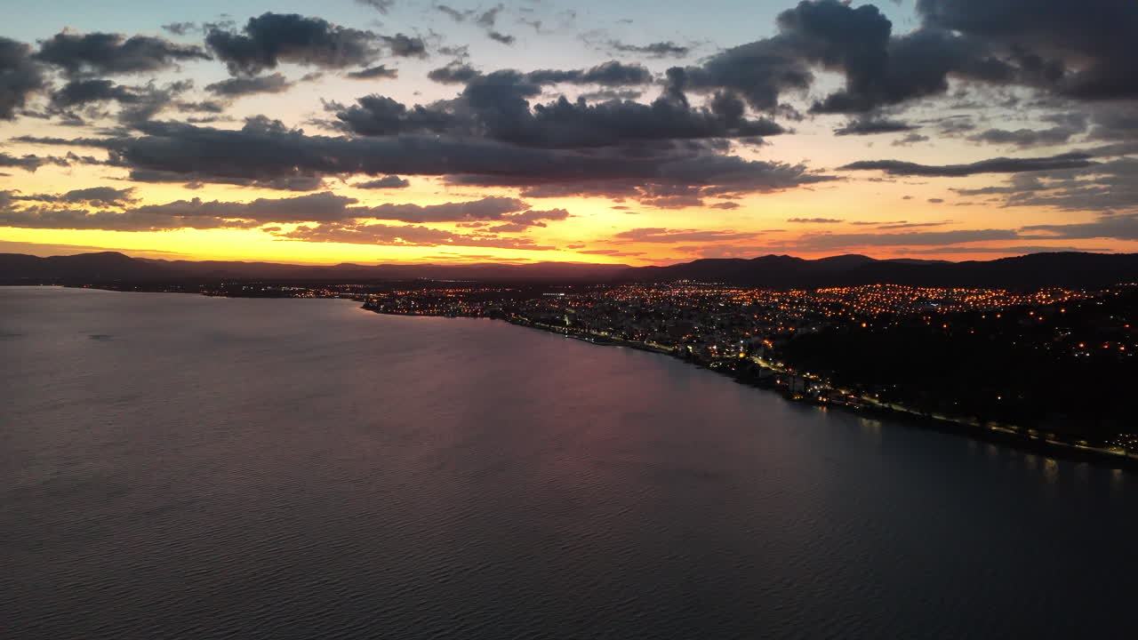 increíble puesta de sol, amanecer en el horizonte de bariloche, luces de la ciudad y cielo nublado, agua en el frente, copia espacio, aérea