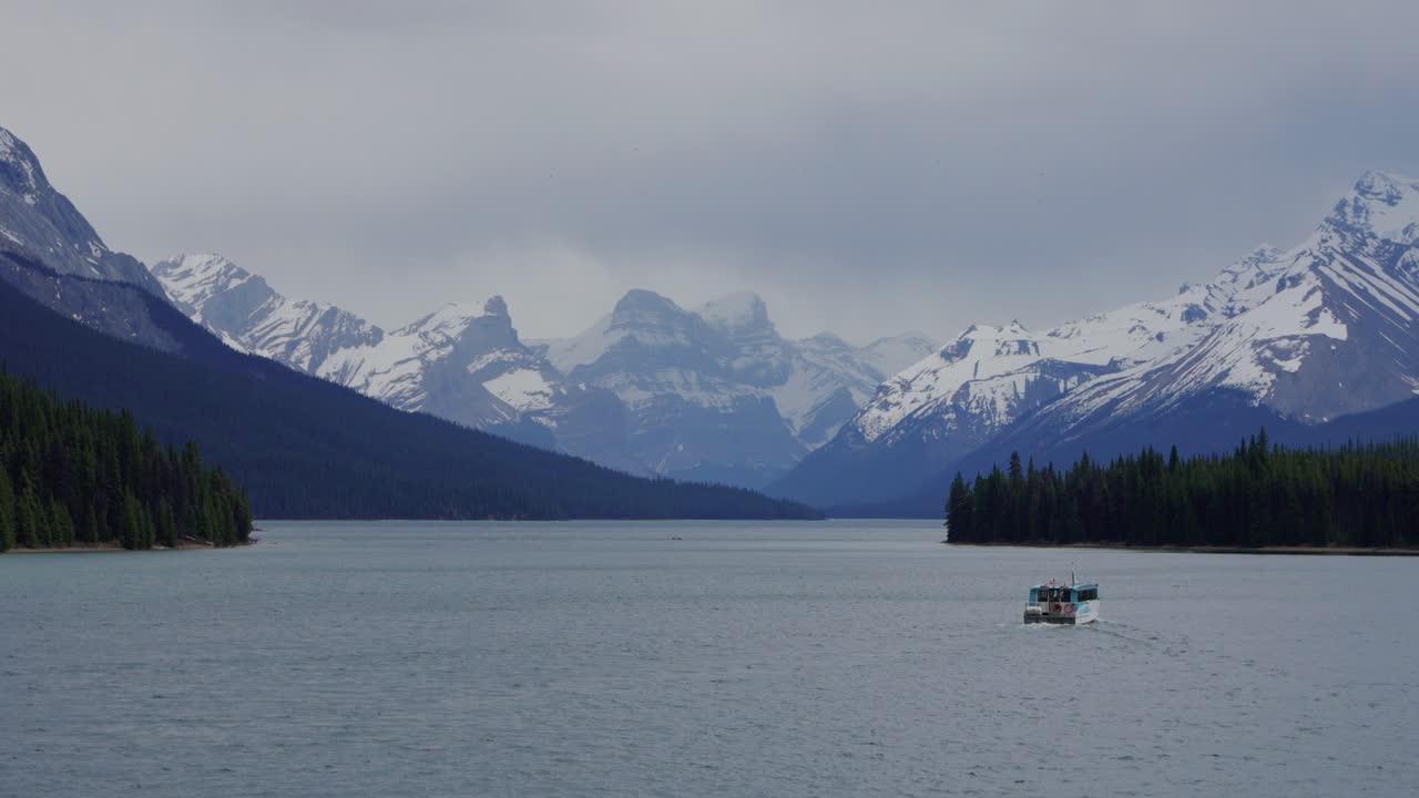 Barca turistica che naviga sul lago Maligne con montagne innevate nel parco nazionale di Jasper, Canada.