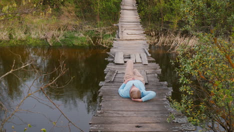 man relaxing on an old wooden bridge over a river