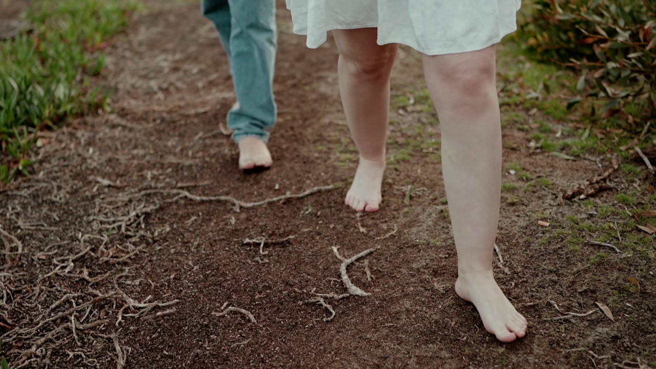 Man and woman walking barefoot on natural dirt path outdoors wearing casual clothes showing relaxed lifestyle and connection