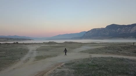 forward drone shot of a girl running towards a lake