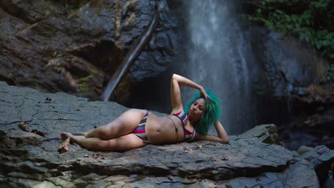 Bikini-girl-laying-on-a-rock-at-the-base-of-a-flowing-waterfall-in-the-Caribbean
