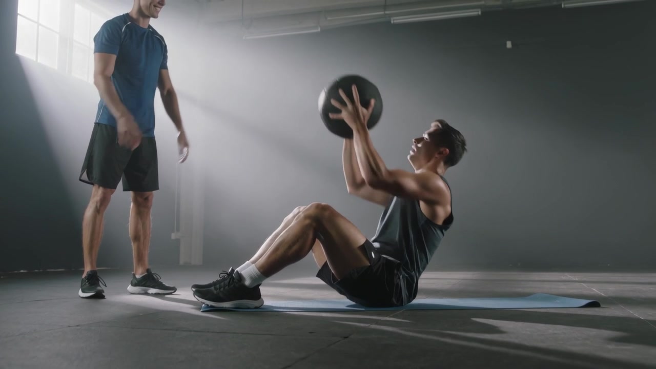 Doing seated man sleeveless weighted situps on blue mat, partner passing medicine ball timing reps