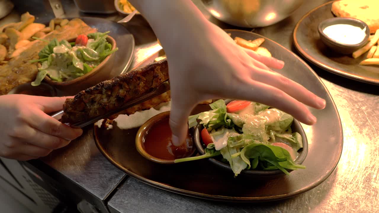 The chef places ribs on a platter with fries and salad