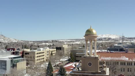 an aerial orbiting shot of a small tower in the middle of a small town overlooking snowy mountains