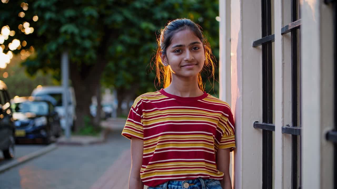 mujer joven de pie al aire libre durante la hora dorada, rodeada de coches estacionados y árboles, tomando el sol en la suave luz de la tarde con una expresión pacífica y contemplativa en el entorno de la calle urbana