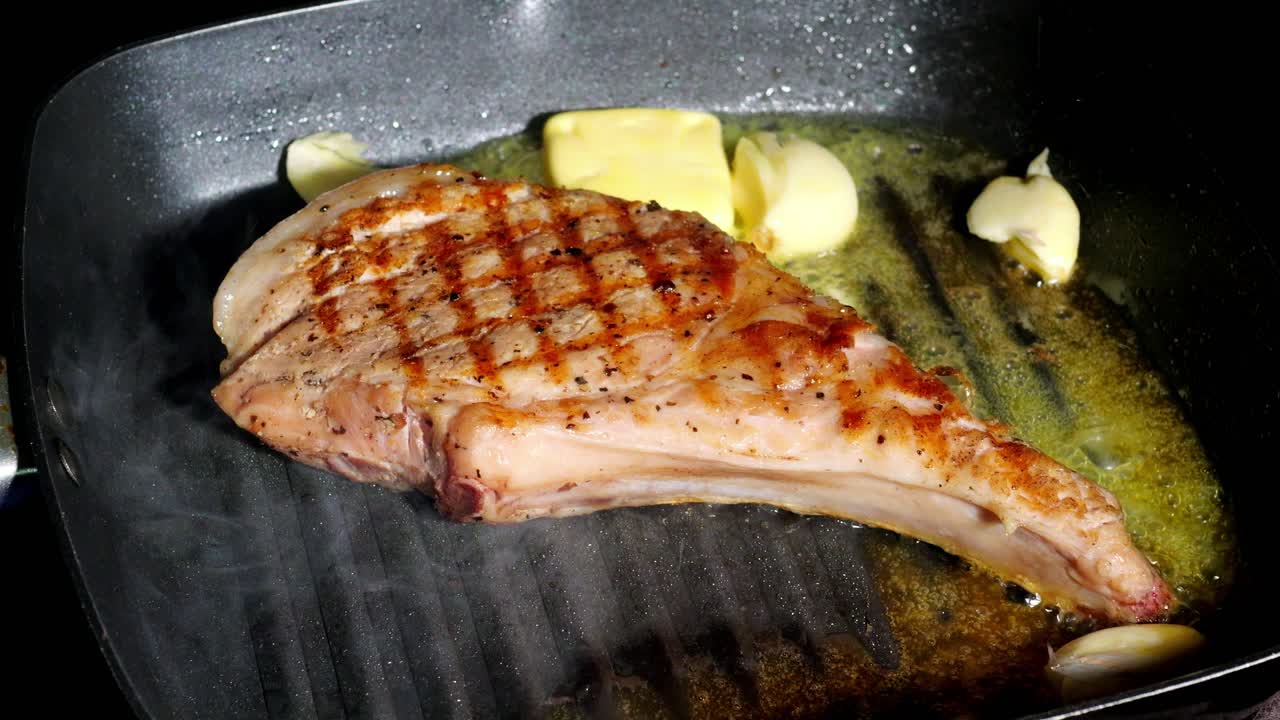 Basting steak-pork chop with butter, rosemary and garlic on hot pan, slow motion