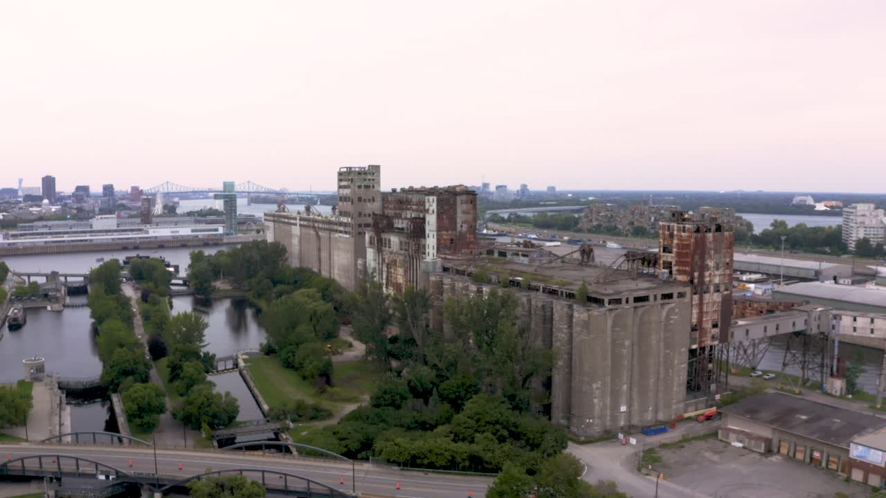 Aerial view of rusted industrial silos with a modern city skyline backdrop. A stunning contrast of urban decay and sleek architecture. Montreal's Old Port docks.
