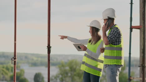 ingenieros diseñadores un hombre y una mujer de pie en el techo de un edificio en construcción y discutir el plan y el progreso de la construcción utilizando una tableta y un teléfono móvil. los constructores modernos discuten la infraestructura del edificio y el área circundante