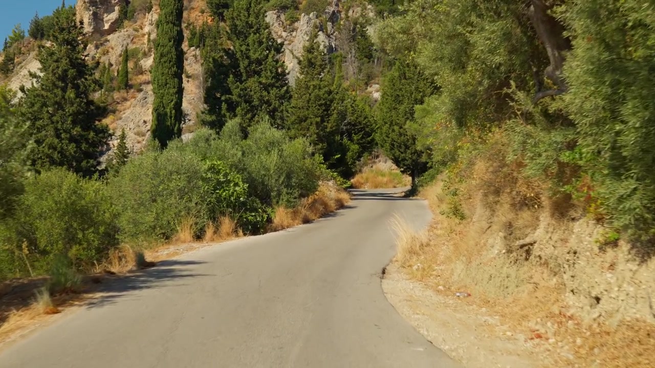 Strada asfaltata vuota che si snoda tra rigogliosi ulivi e colline rocciose in una giornata di sole