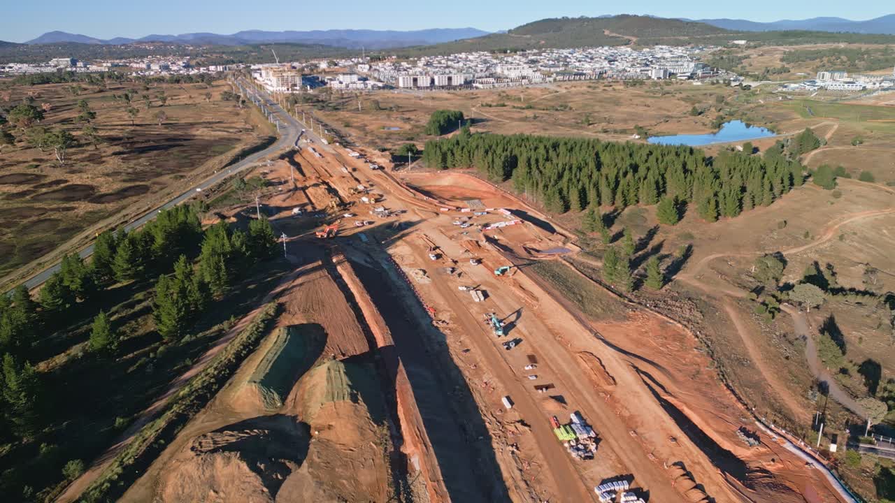 Aerial drone view over a highway being built in Canberra with newly constructed houses of a nearby suburb in the background.