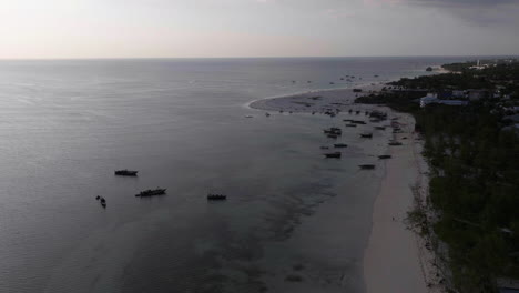 Barcos-Pesqueros-Amarrados-En-La-Playa-Y-El-Pueblo-Pesquero-De-Zanzíbar-Por-La-Noche,-Tanzania.