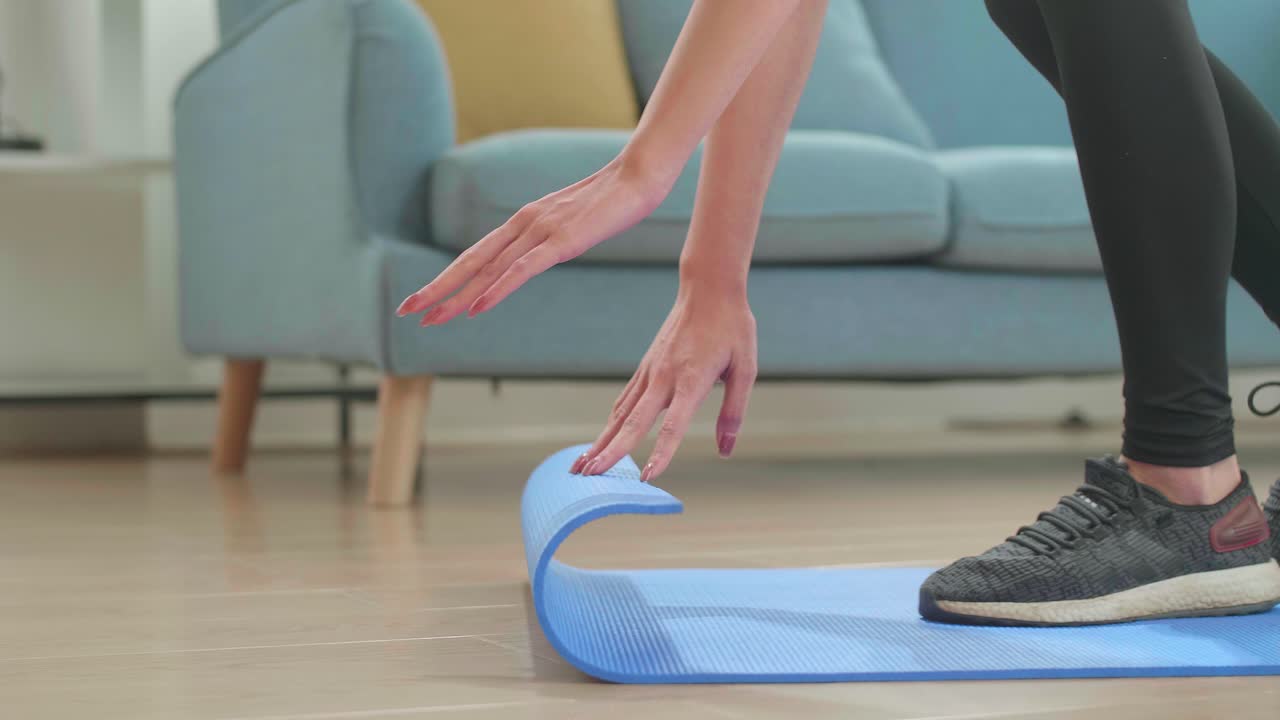 mujer asiática enrolla una alfombra de yoga para la preparación, mujer trabaja haciendo ejercicio de yoga en la sala de estar en casa