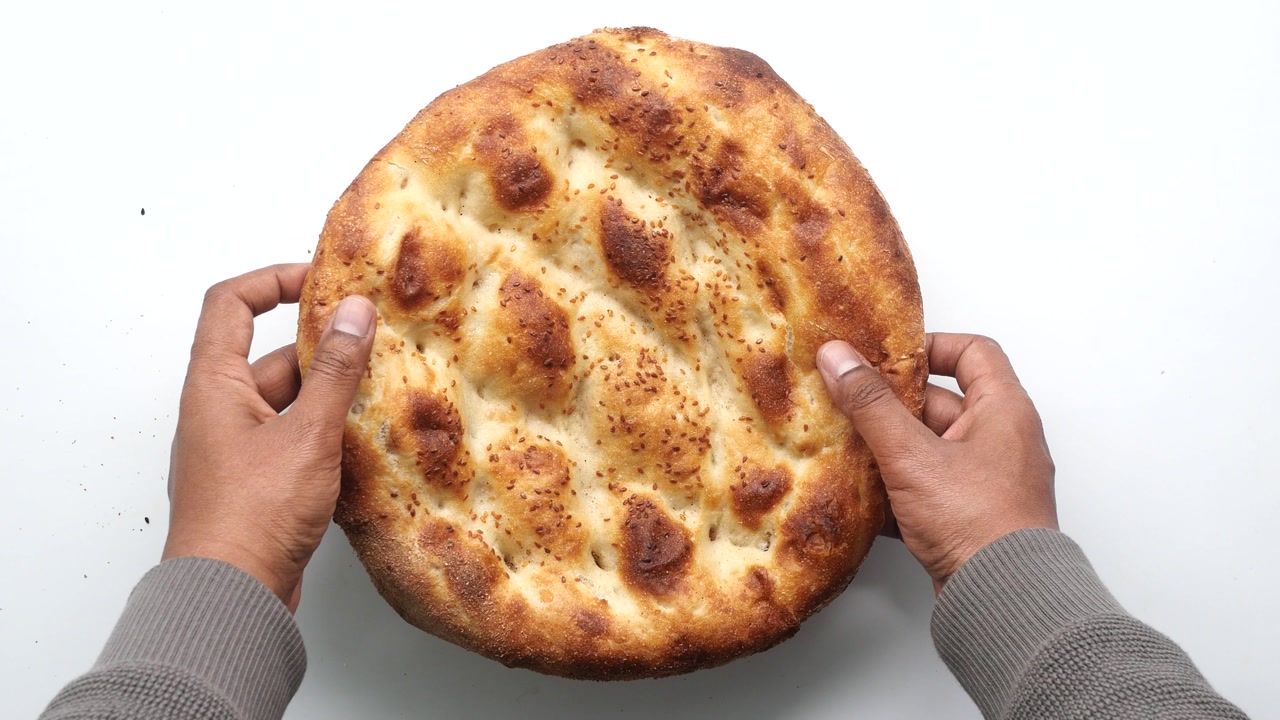 Hands Gently Touching Freshly Baked Flatbread with Sesame Seeds