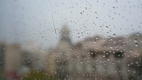 a view of slow-motion close-up view of heavy rain as raindrops land on a window glass, with an urban city landscape in the background