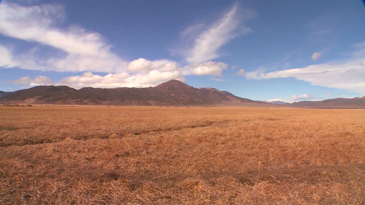 las nubes se mueven sobre una montaña distante detrás de un campo en timelapse