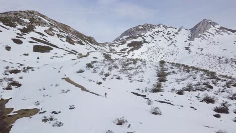 Aerial-view-of-man-hiking-to-top-of-snow-capped-mountains-in-winter