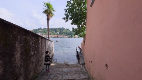 a traveler strolls down a charming narrow street in san giulio, leading to the picturesque lake orta on a tranquil day.