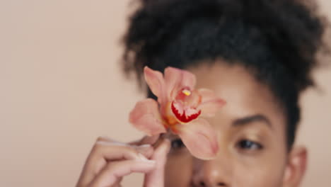 retrato de belleza hermosa mujer afroamericana posando juguetonamente con una flor de orquídea tocando una piel sana disfrutando de la suave fragancia de la esencia natural concepto de cuidado de la piel