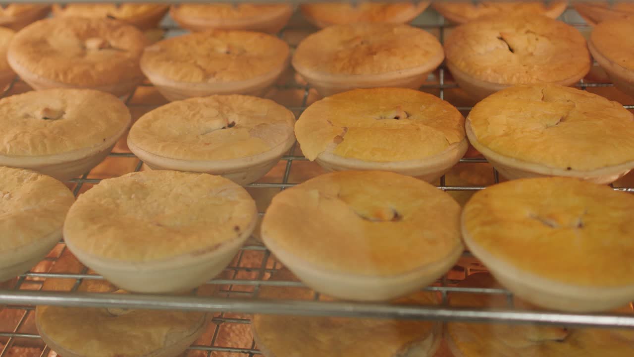 Golden meat pies arranged on metal racks behind glass in warmly lit bakery display case