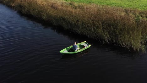 Circulating-drone-shot-with-man-on-fishing-boat-who-are-fishing-in-the-river-near-reeds