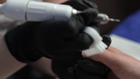 manicurista usando guantes usando una herramienta giratoria para empujar hacia atrás las cutículas de un cliente
