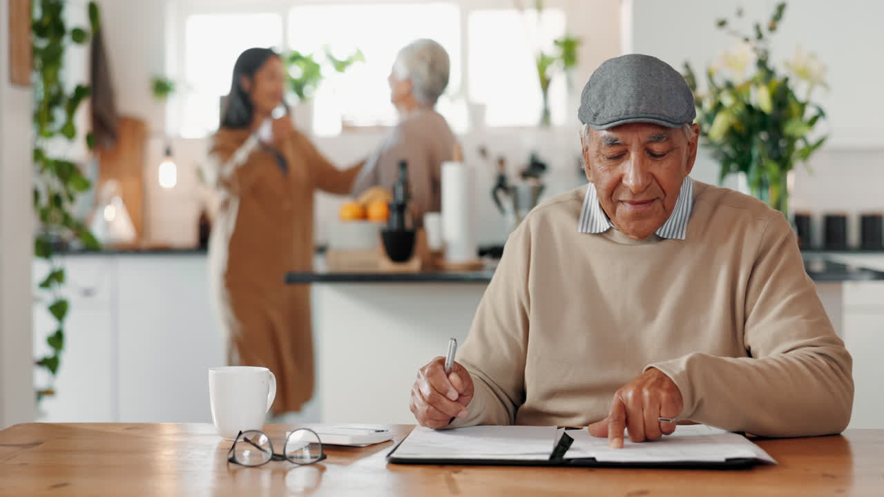 un hombre sentado en una mesa en la cocina, escribiendo en una pieza de papel